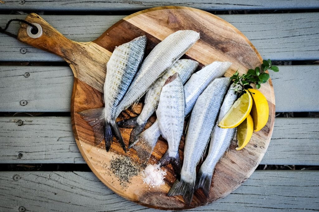 headless fishes with sliced of lemons on brown wooden chopping board